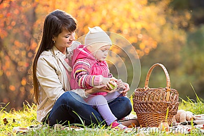 Kid and mother sit with apples basket outdoors in autumnal park Stock Photo